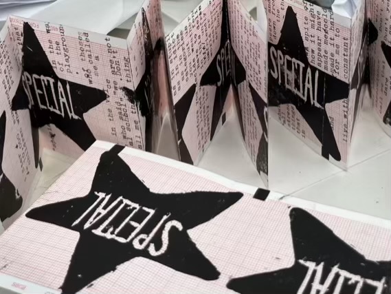 On paper with a small red grid multiple roughly printed black stars with the word “special” carved out of them appear. Some of these feature printed text underneath related to the experience of growing up disabled and the artists feeling about being called “special”