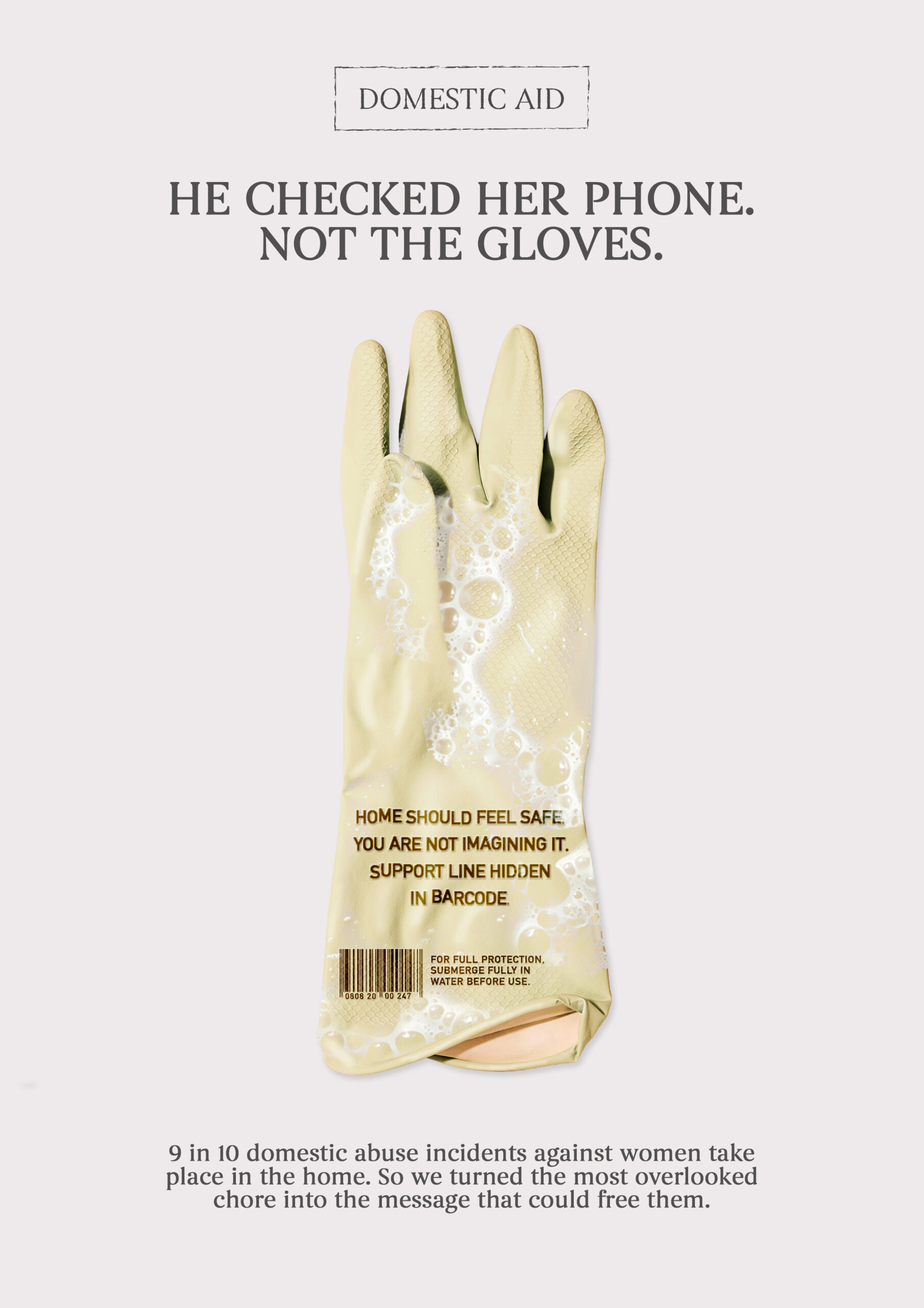 A Domestic Aid campaign poster showing a single washing up glove with soapy water revealing the hidden message "Home should feel safe. You are not imagining it. Support line hidden in barcode." The headline reads "He checked her phone. Not the gloves."